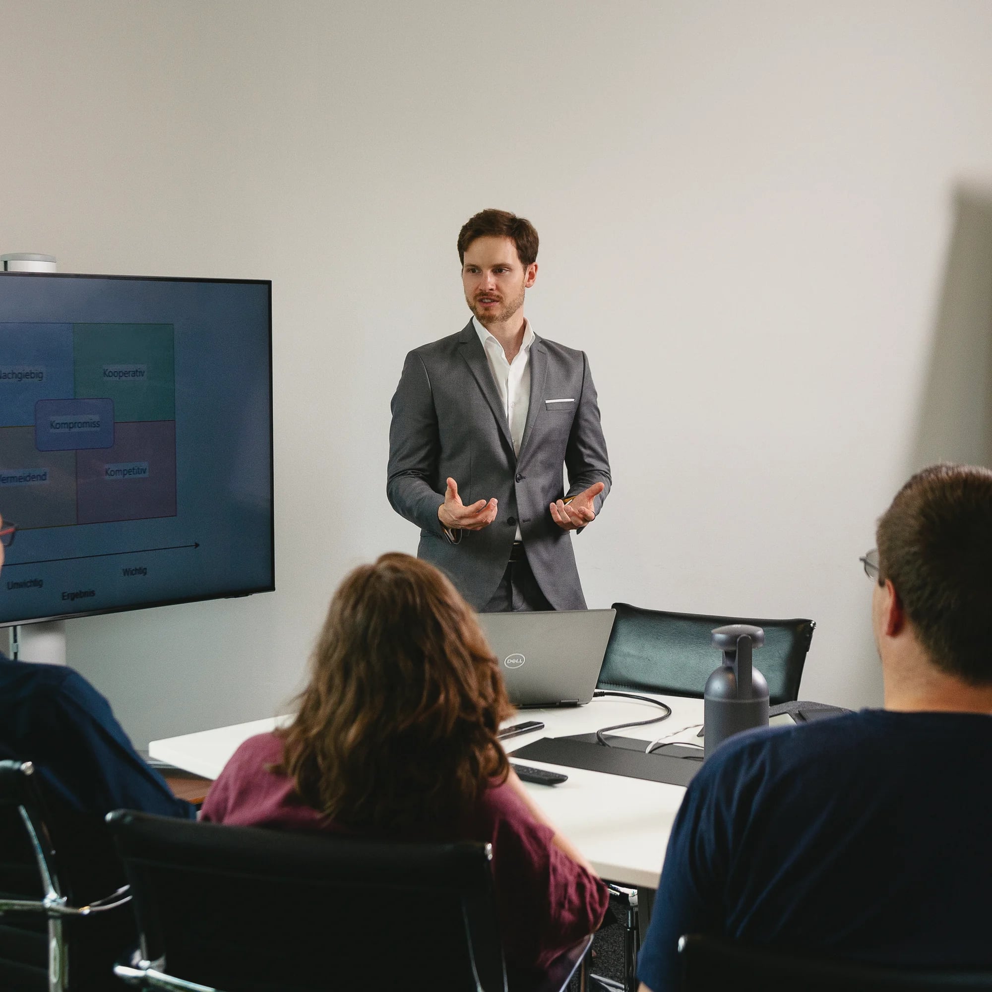 Seminarleiter erklärt der Gruppe am Bildschirm die Matrix der Verhandlungsstile; die Teilnehmenden sitzen am Konferenztisch.
