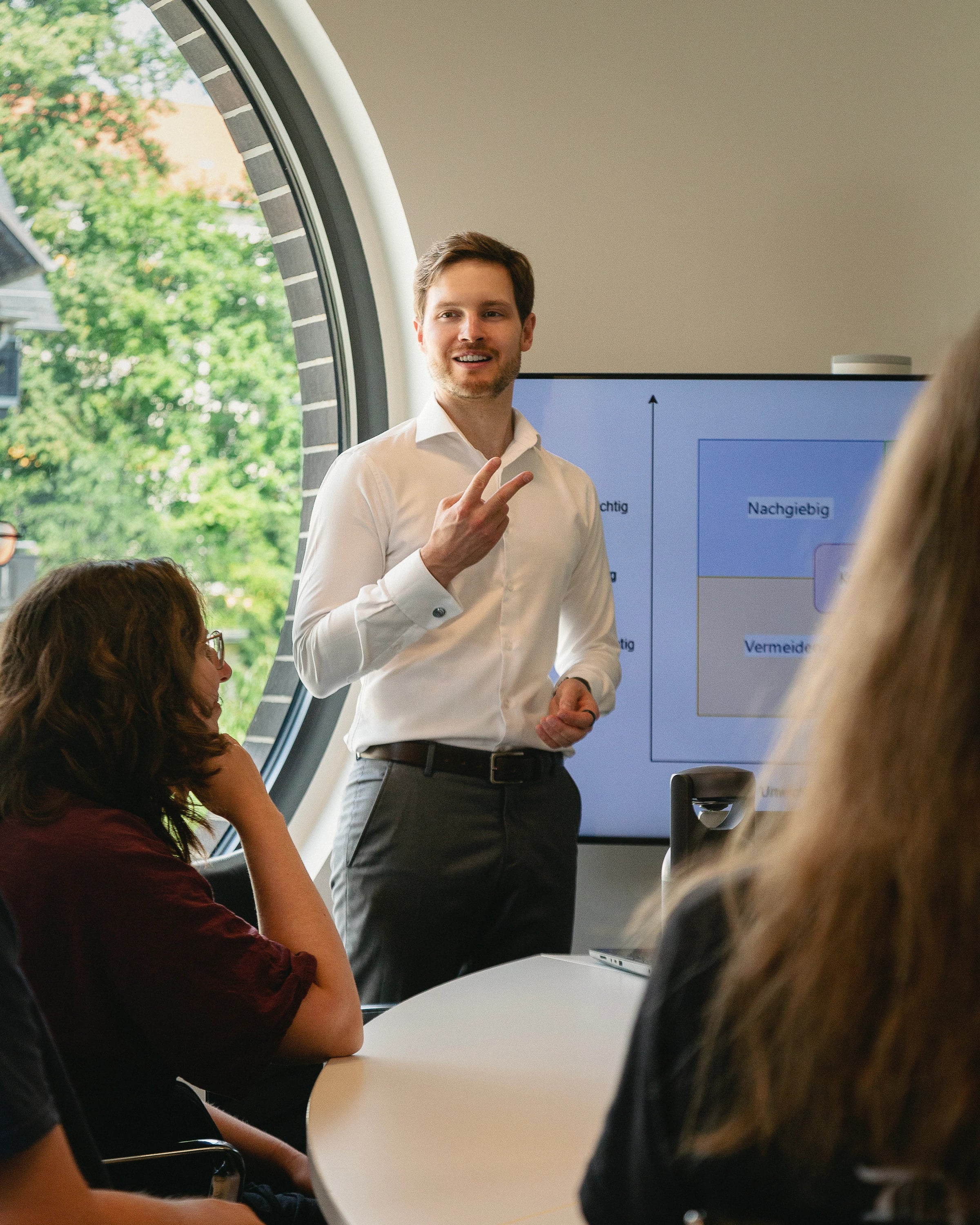 Seminargruppe am Konferenztisch; der Seminarleiter erklärt am Bildschirm die vier Verhandlungsstile.